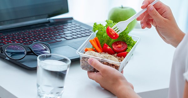 Up close image of person eating salad at their desk