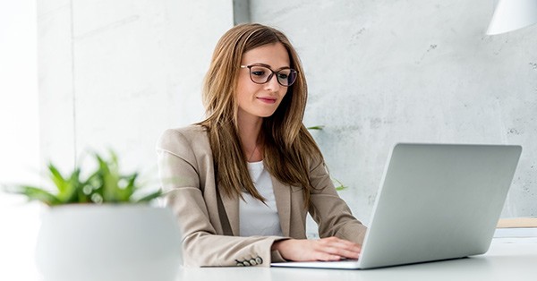 Woman sitting at desk on laptop with a plant next to her